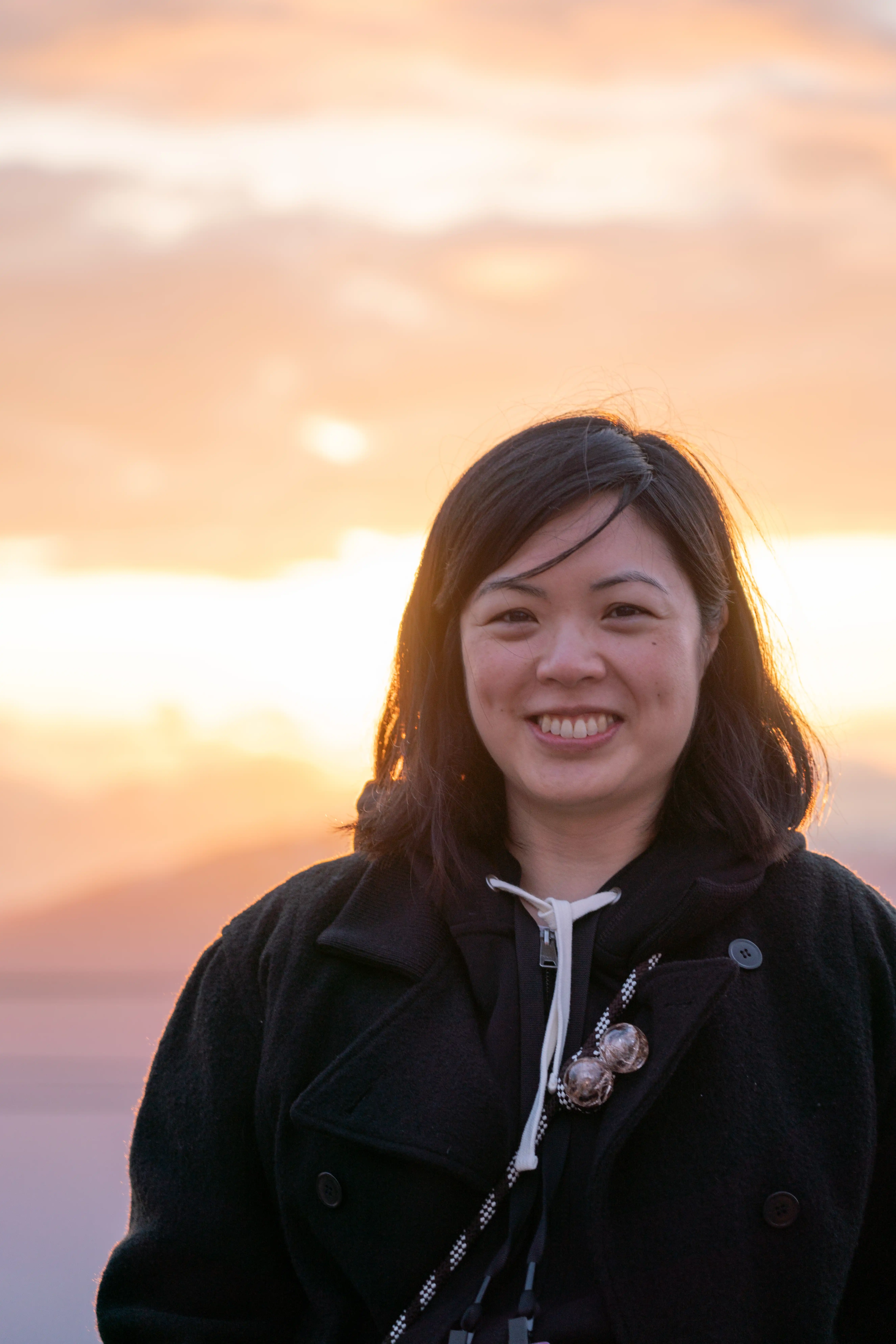 A photo of an Asian woman with black hair smiling in front of a light-filled sky